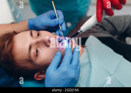 Odontoiatria. Dentista e paziente. Guarnizione indurente leggera. Lampada da denti UV e vetro protettivo arancione. Foto Stock