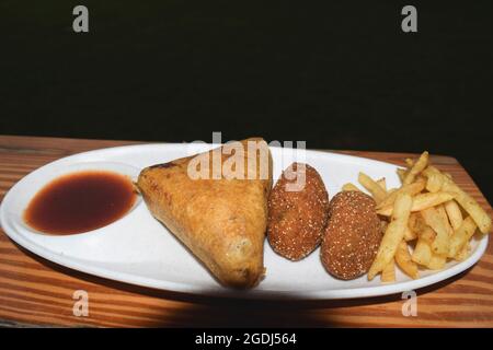 Deliziosi spuntini indiani assortiti serviti con chutney di datteri in piatto. Pakoda di pane triangolare, cotolette di formaggio Cottage con patatine fritte. Foto Stock