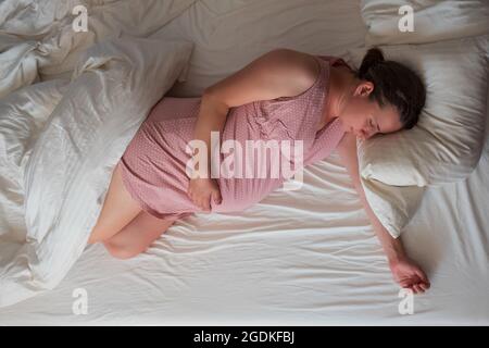 Donna caucasica incinta che dorme in abiti rosa a letto Foto Stock