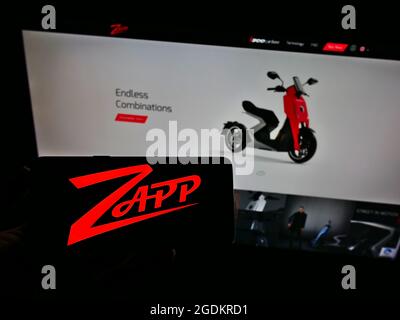 Persona che tiene smartphone con il logo della società di moto elettrica Zapp Scooters Ltd. Sullo schermo di fronte al sito web. Mettere a fuoco il display del telefono. Foto Stock