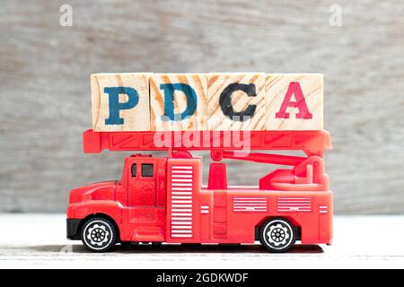 Carrello giocattolo a scala antincendio tenere il blocco di lettere in parola PDCA (Plan, do, Check, Act) su sfondo di legno Foto Stock