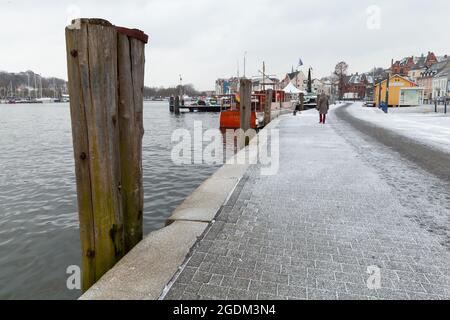 Flensburg, Germania - 8 febbraio 2017: Vista costiera di Flensburg con colonne di ormeggio in legno in piedi in acqua, la gente comune cammina la strada Foto Stock