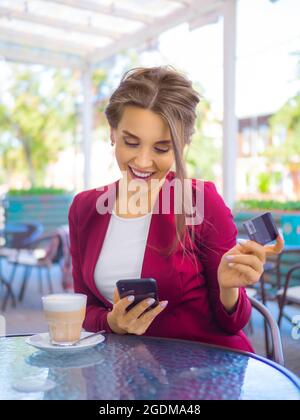 Donna sorridente felice con smartphone e carta di credito durante la pausa caffè. Concetto di shopping online e di trading online. Foto Stock
