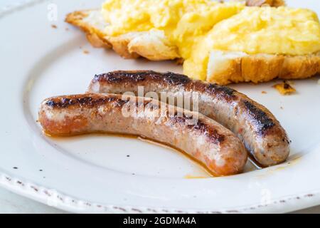 Salsiccia di merguez con uova strapazzate e croissant nel piatto della colazione. Pronto a mangiare. Foto Stock