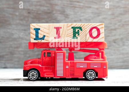 Toy Fire ladder Truck tenere il blocco di lettere in LIFO (abbreviazione di last in first out) parola su sfondo di legno Foto Stock