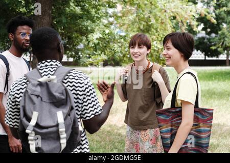 Gruppo di giovani amici che si levano in piedi e si comunicano tra loro durante il loro incontro nel parco Foto Stock
