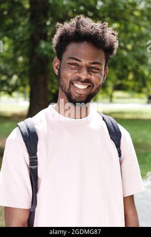 Ritratto di felice studente africano con zaino dietro la schiena sorridente a macchina fotografica mentre si alza in piedi all'aperto Foto Stock