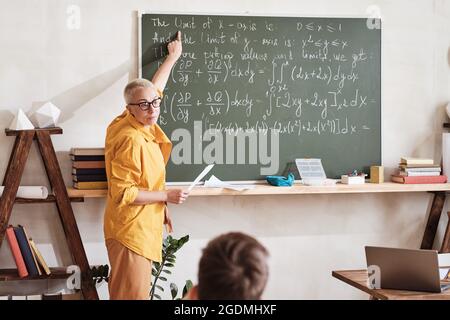 Insegnante in piedi alla lavagna e indicando la formula matematica che spiega materiale agli studenti all'università Foto Stock