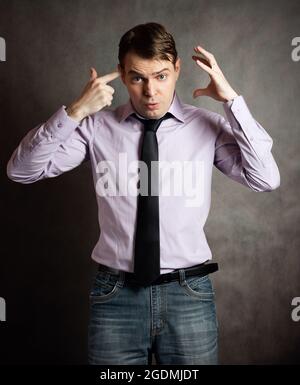 Ritratto di pensieroso Giovane Uomo in camicia rosa scuro e cravatta, contro uno sfondo scuro. Foto Stock