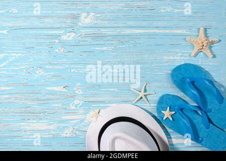cappello bianco paglia, infradito in gomma blu e stelle marine su sfondo di legno blu Foto Stock