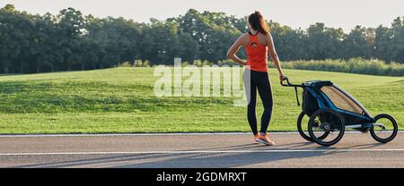 La madre attiva nello sport usa il passeggino da jogging per correre al parco. Donna felice che si diverte mentre si allenano all'aperto. Pubblicità jogging passeggino Foto Stock