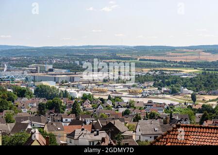 Un villaggio con molti alberi e una fabbrica sulla riva del fiume sullo sfondo di colline e campi, vista aerea. Foto Stock