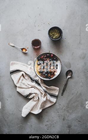 Vegano sana prima colazione. Flat-lay di quinoa oat granola cocco ciotola di yogurt con frutta, miele, sementi, dadi, bacche su cemento grigio sfondo tabella Foto Stock