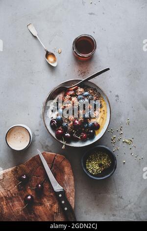 Vegano sana prima colazione. Flat-lay di quinoa oat granola cocco ciotola di yogurt con frutta fresca, sementi, dado, bacche e tazza di caffè sulla backgroun grigio Foto Stock