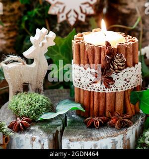 Candela decorata con bastoncini di cannella, muschio, foglie d'edera e cervi di legno - bella disposizione di Natale naturale. Foto Stock