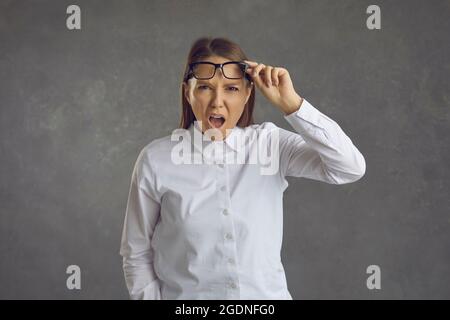 Donna stupita toglie i suoi occhiali e guarda da sotto la fronte con la sua bocca aperta. Foto Stock