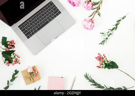 Splendido spazio di lavoro con computer portatile, notebook, scatola di carta e fiori rosa su sfondo bianco. Vista dall'alto. Disposizione piatta. Foto Stock