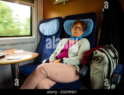Donna di mezza età seduta accanto alla finestra nel compartimento del treno che dorme Foto Stock
