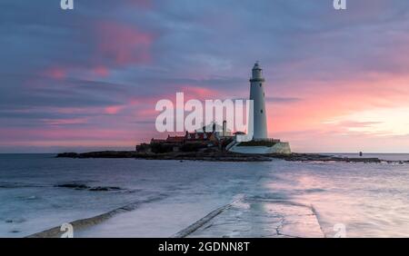 Il faro di St Mary a Whitley Bay si riflette nelle nuvole in una splendida alba e la strada rialzata inizia a manifestarsi quando la marea si spegne Foto Stock