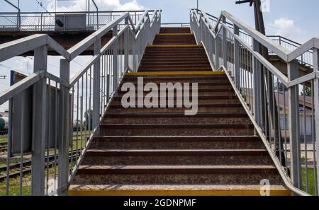 Ponte ferroviario con scalini, con scalini impressionanti in prospettiva. Attraversamento pedonale in alto. Ponte scale che collegano una piattaforma a un'altra presso Foto Stock