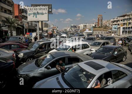 Beirut, Libano. 14 agosto 2021. I veicoli si accodano fuori da una stazione di servizio a Beirut mentre i soldati dell'esercito libanese controllano l'ingresso per frenare l'accaparramento di carburante, come il capo della banca centrale Riad Salameh ha annunciato questa settimana che non sarebbe più in grado di sovvenzionare le importazioni di carburante con un tasso di cambio fisso in dollari. Sabato scorso il caos ha colpito le stazioni di benzina del Libano, colpito dalla crisi, mentre l'esercito libanese e la polizia di sicurezza interna si sono inforzati a costringere i proprietari a vendere il carburante che avevano immagazzinato alla popolazione. Credit: Marwan Naamani/dpa/Alamy Live News Foto Stock