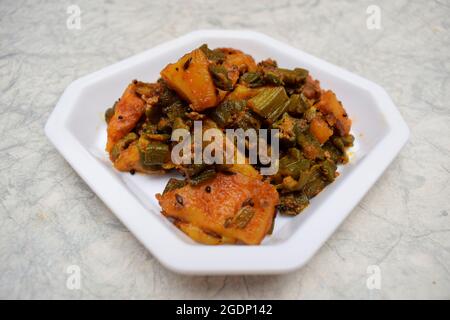 Vista dall'alto del bhindi aloo sabji o del ladyfinger okra miscelato con patate al curry vegetale indiano servito in piatto bianco su sfondo bianco. Gustoso e delizioso Foto Stock