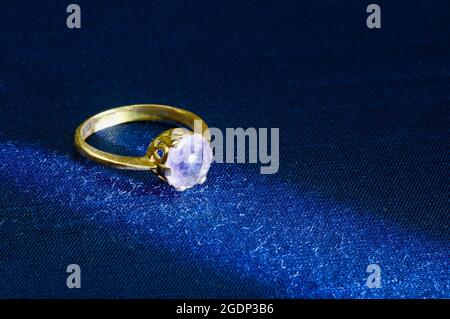 Un anello d'oro con ametista su un tappetino blu, messa a fuoco selezionata Foto Stock