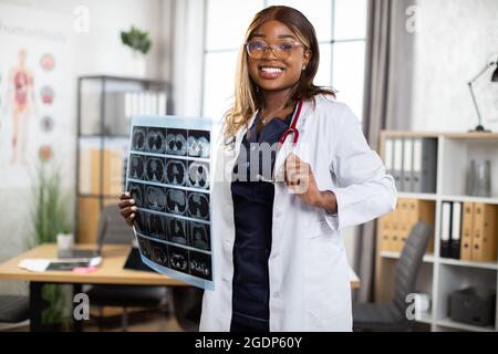 Apparecchiature mediche, radiologia, persone e concetto di occupazione. Ritratto di una donna brava sorridente bravo medico gp nero, che posava a macchina fotografica nel suo moderno ufficio privato con MRI scansione in mani Foto Stock