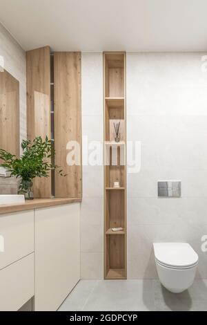 Moderno design minimalista degli interni del bagno con piastrelle in pietra ecru e mensola nascosta in legno per accessori da bagno Foto Stock