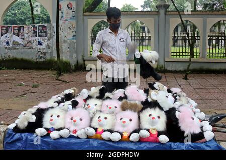 Non esclusivo: DHAKA, BANGLADESH - AGOSTO 13: Una persona del Bangladesh, indossa una maschera protettiva per il viso mentre offre figure di peluche ai visitatori sul lato Foto Stock