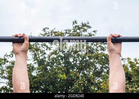 Sport all'aperto. Un uomo si tira su una barra orizzontale nel parco. Foto Stock