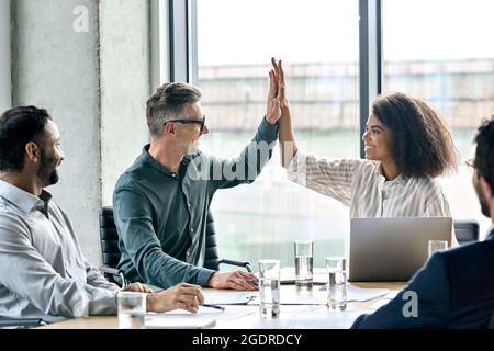 Felice gente internazionale d'affari che dà alto cinque al tavolo della sala riunioni. Foto Stock