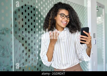 Gioioso giovane business manager afroamericano che usa il telefono in piedi in ufficio. Foto Stock