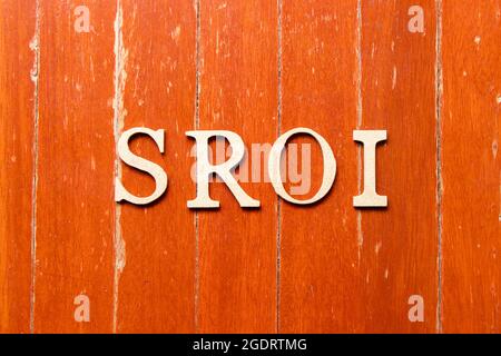 Lettera alfabetica in parola SROI (abbreviazione di Social Return on Investment) sul vecchio colore rosso sfondo della piastra in legno Foto Stock