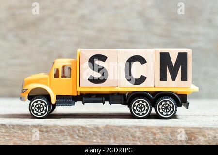 Carrello giocattolo tiene un blocco di lettere alfabetiche in parola SCM (abbreviazione di Supply Chain Management) su sfondo di legno Foto Stock