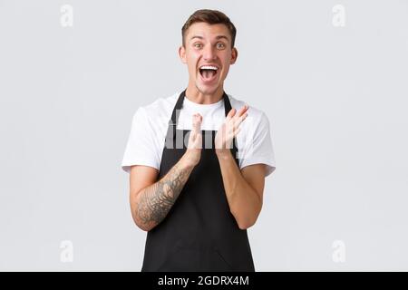 Dipendenti, negozi di alimentari e caffetteria. Il barista felice impressionato ed eccitato in grembiule nero ha clap le mani per la classe principale sulla preparazione del caffè Foto Stock