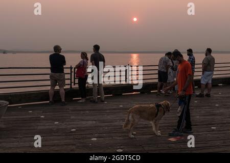 Seattle, Stati Uniti. 14 ago 2021. Persone che visitano il Molo 56 mentre la costa occidentale finisce l'onda di calore. Spesso arancione clima fuoco fumo rimane sulla città. I Seattleiti hanno dovuto imparare a vivere con i cieli ormai regolarmente affumicati nella seconda parte delle estati. Gli incendi legati ai cambiamenti climatici infuriano annualmente nel PNW, riducendo significativamente la qualità dell'aria e riducendo la qualità della vita per molti. James Anderson/Alamy Live News Foto Stock