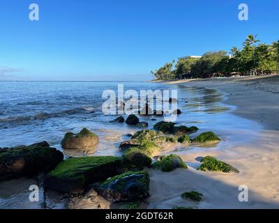 Le onde oceaniche lambiscono le coste dorate e le rocce disseminate di alghe di Ka'anapali Beach a Lahaina, Hawaii. Foto Stock