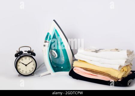 Sveglia, ferro da stiro moderno bianco e blu, asciugamani sul tavolo. Stirare i vestiti su sfondo bianco. Foto Stock
