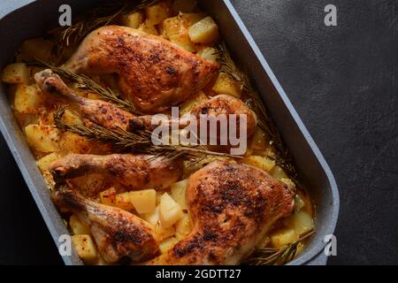 Quarti di coscia di pollo al forno e bastoncini di pollo conditi con aglio ed erbe con patate in un piatto da forno Foto Stock