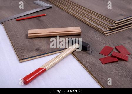 Tavole di pavimento laminato e attrezzature o attrezzi per installarli, martello, distanziatori, matita e righello con barra angolare. Messa a fuoco selettiva. Foto Stock