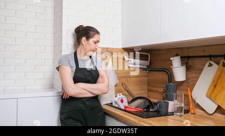Donna stanca guarda un mucchio di piatti sporchi in cucina Foto Stock