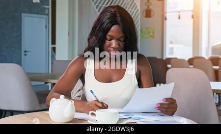 Donna afroamericana lavora con diagrammi al tavolo in caffetteria Foto Stock