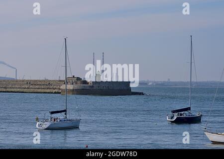 Splendida vista serale di yacht in barca sull'acqua presso i porti di Dun Laoghaire con il faro del West Pier e i camini di Poolbeg, Dublino, Irlanda Foto Stock