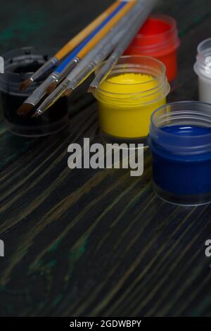 Set di gouache per la scuola. Le barattoli di vernice giacciono sulle tavole di pino. Nelle vicinanze sono presenti pennelli. Foto Stock