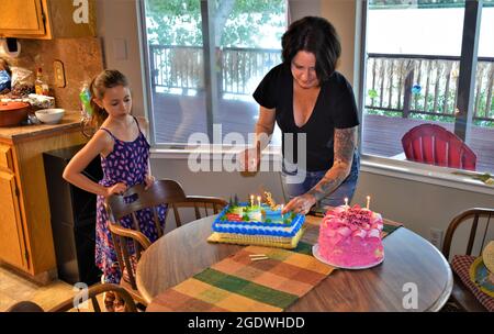 Donna e sua figlia che mettono tocchi sulla torta di compleanno del papà per una festa a sorpresa più tardi Foto Stock