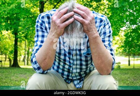 Vecchio depresso seduto sulla panchina in un parco. Uomo infelice Foto Stock