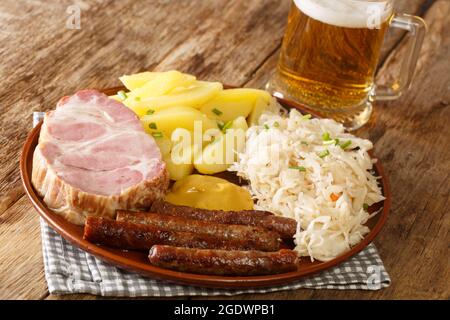 Salsiccia rustica di cibo tedesco, collo di maiale Kassler, crauti, senape, patate bollite e chiocciole di birra leggera sul tavolo. Orizzontale Foto Stock