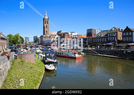 Roermond, Paesi Bassi - 9 luglio. 2021: Vista sull'affollato canale d'acqua olandese con paesaggio urbano e la vecchia torre della chiesa contro il cielo estivo blu Foto Stock