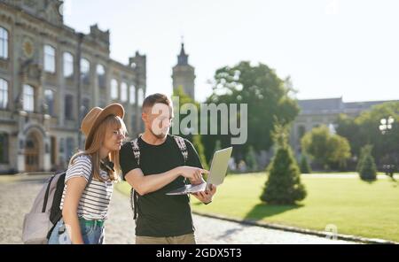 Felice coppia di successo degli studenti utilizzando un computer portatile per l'istruzione online. Due simpatici studenti internazionali, di sesso maschile e femminile, con zaini che usano il notebook presso il campus universitario. Foto di alta qualità Foto Stock